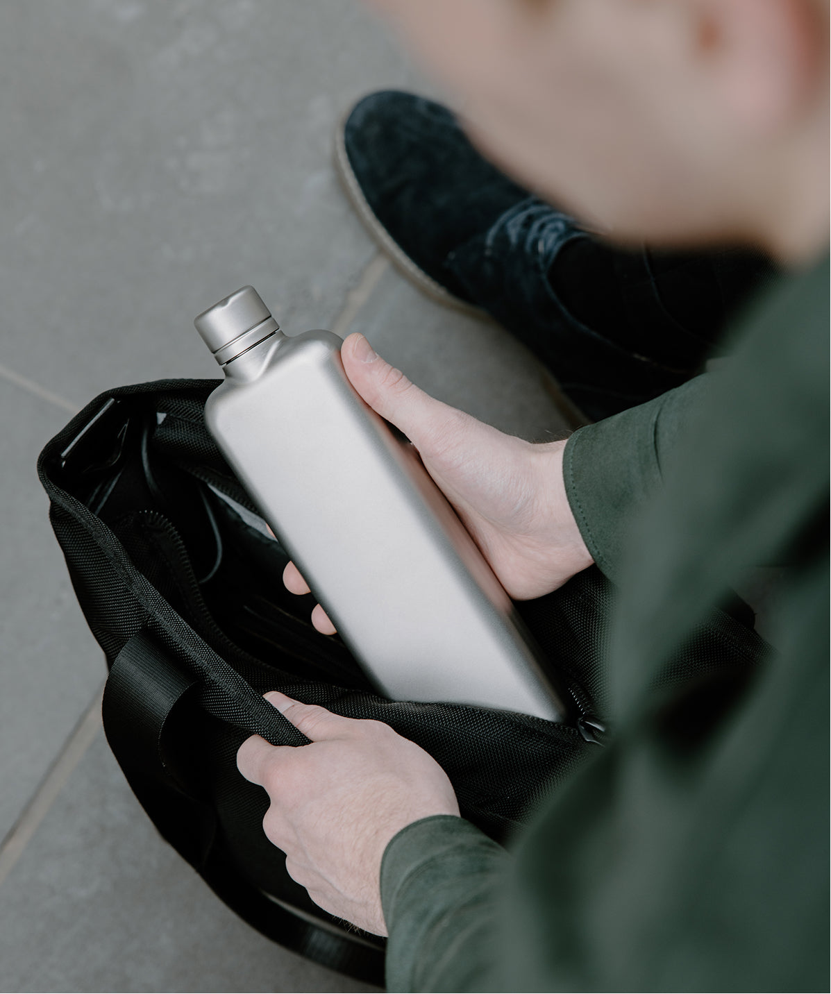 Botella de acero gris con forma plana que encaja perfectamente en el bolsillo lateral o frontal de una mochila.