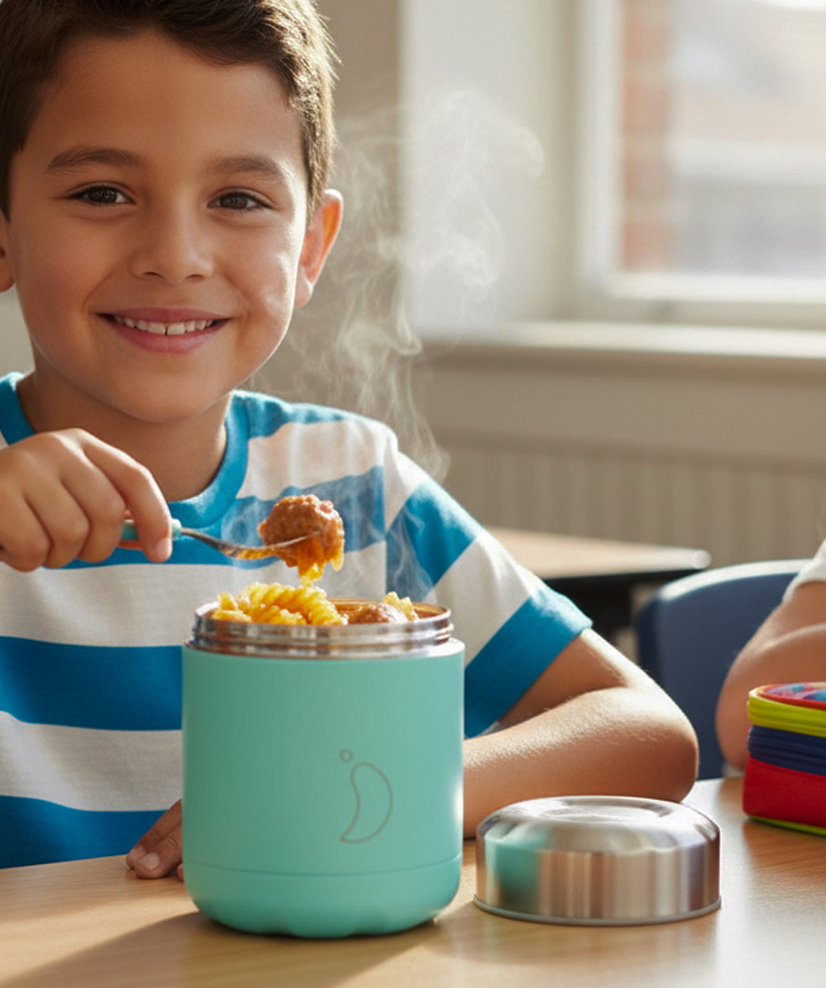 Niño sonriendo comiendo con cuchara en un parque con el termo de sólidos Chilly's Mate Menta 300ml. Termo de comida infantil, mantiene caliente hasta 6 horas.