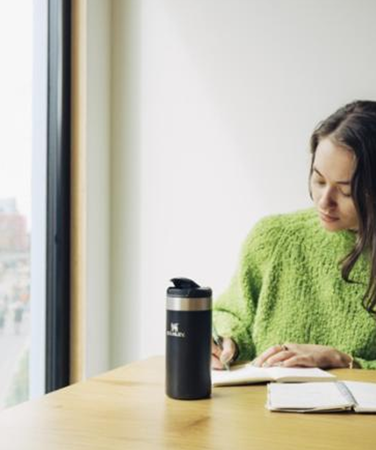 Chica en escritorio con Vaso Stanley AeroLight™ Transit Mug negro 350ml. Vaso de acero inoxidable ideal para teletrabajo.