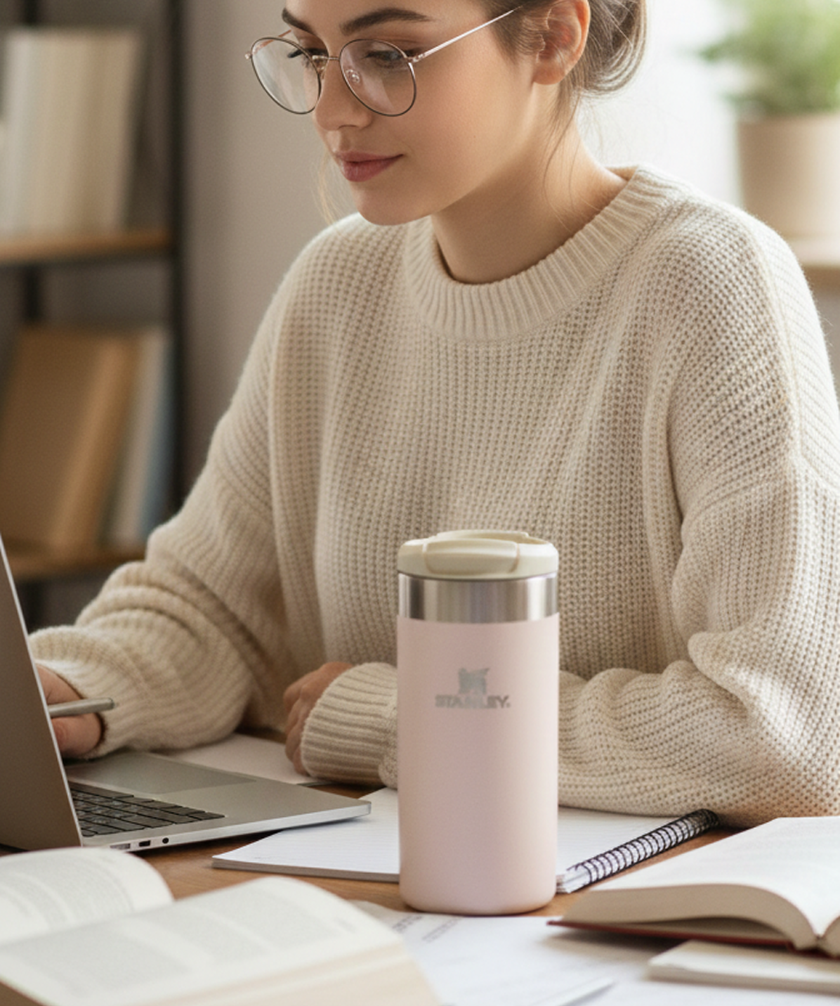Chica trabajando en escritorio con Vaso Stanley AeroLight™ Transit Mug rosa cuarzo. Vaso de acero inoxidable para café en la oficina.