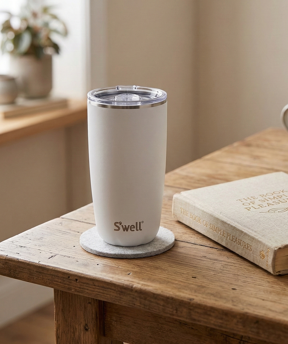 Vaso S'well Tumbler Stone Moonstone blanco en una mesa junto a un libro para un café de lectura.